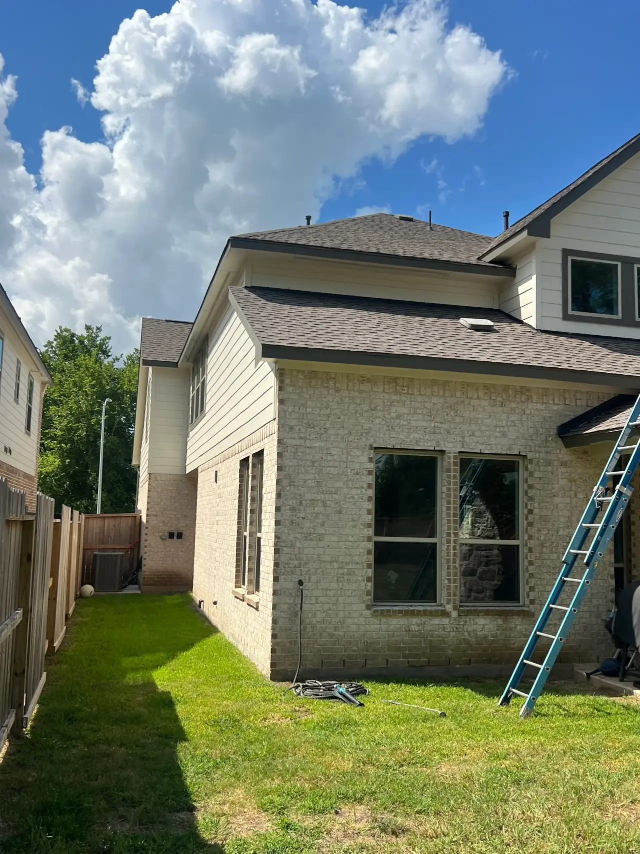 Two-story brick home with a ladder against the lower roof during gutter work
